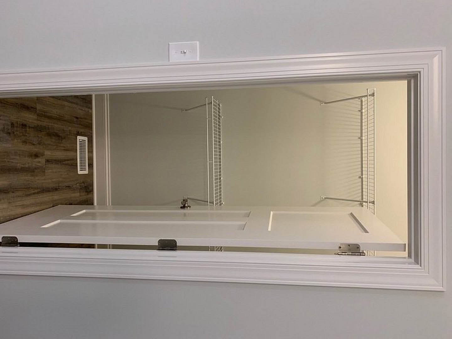 White paneled door open to a bathroom with rectangular mirror, white sink, and window; wall vent and light switch visible; white metal ladder mounted on wall near staircase.