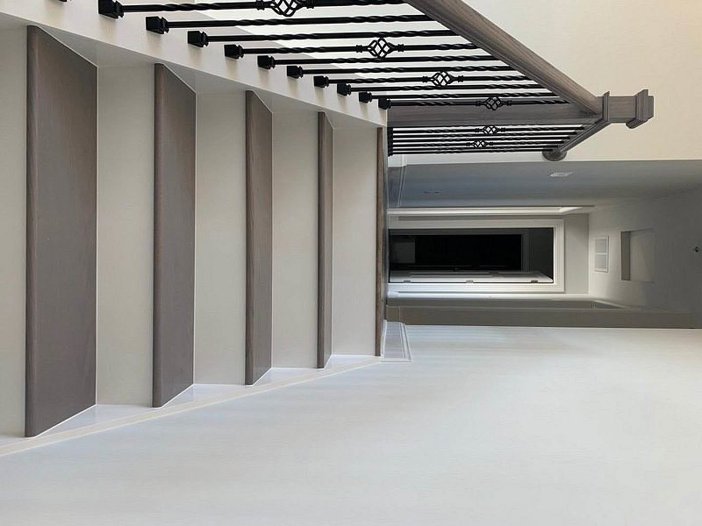 Modern staircase with black metal railings, large window, white walls, brown floor trim, and grey accent wall