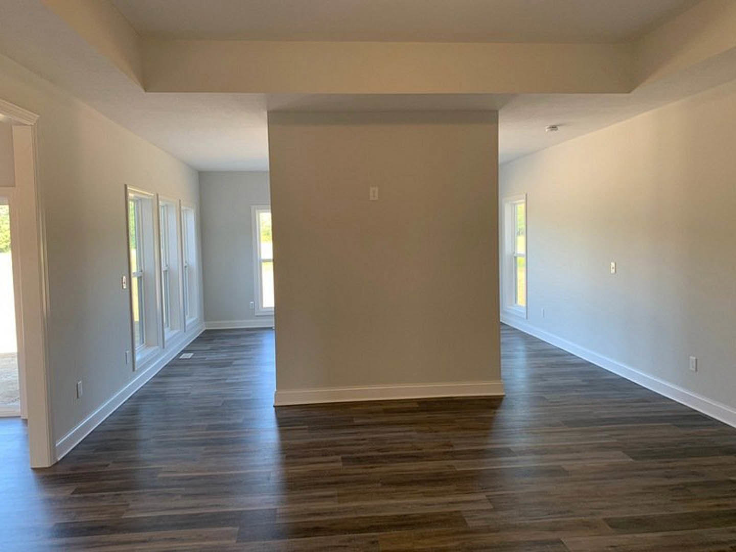 Wood flooring in a room with white plaster walls, light switch, and sunlight streaming through a nearby window.