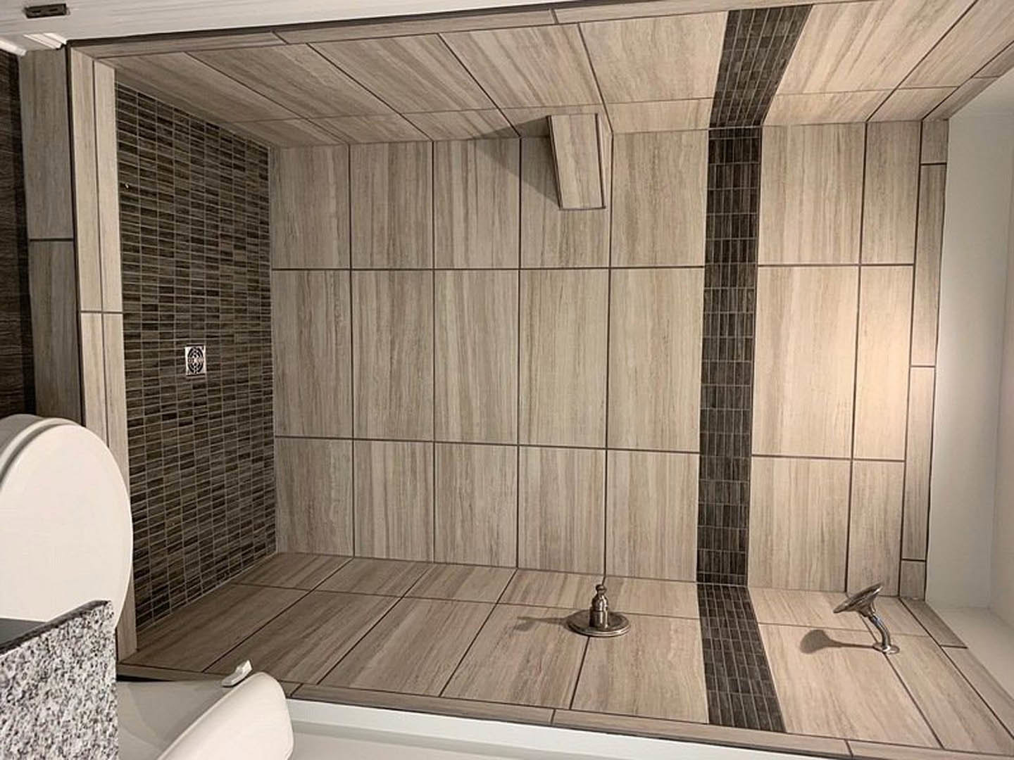 Shower with gray tile walls, white bathtub, and chrome fixtures in a modern bathroom