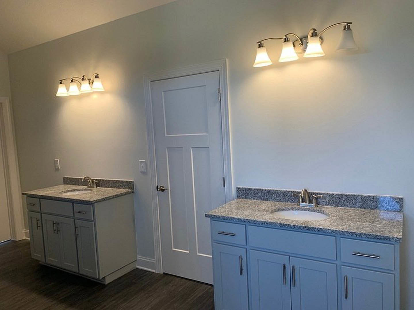 Bathroom with marble countertop and undermount sink, silver faucet, white cabinetry, tile backsplash, two modern light fixtures above mirror, white door with silver handle