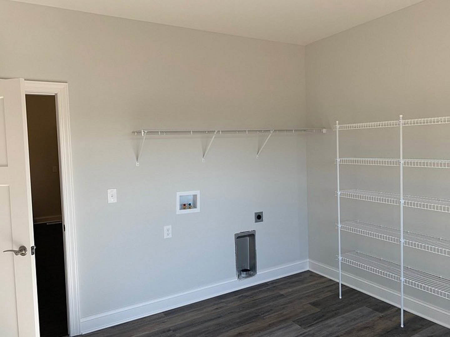 White built-in shelves along a plaster wall, light wood flooring, and a doorway leading to an adjacent room.