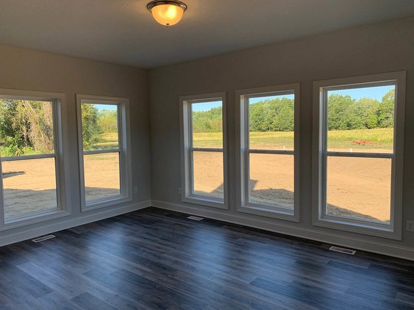 Spacious room featuring dark wood flooring, multiple large windows, and views of green fields and trees outside