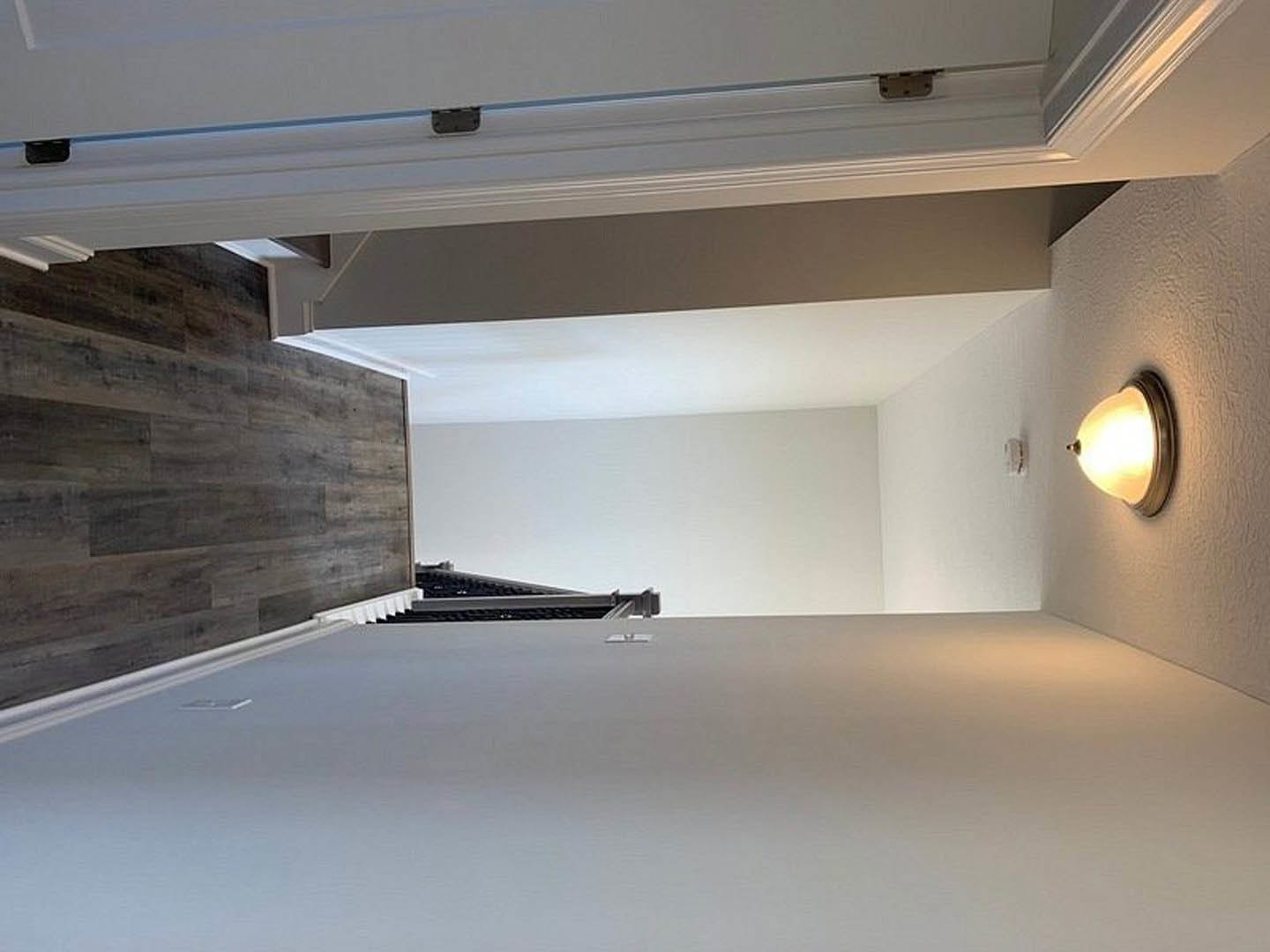Hallway with wood flooring, white plaster walls, and a modern ceiling light fixture illuminating the space