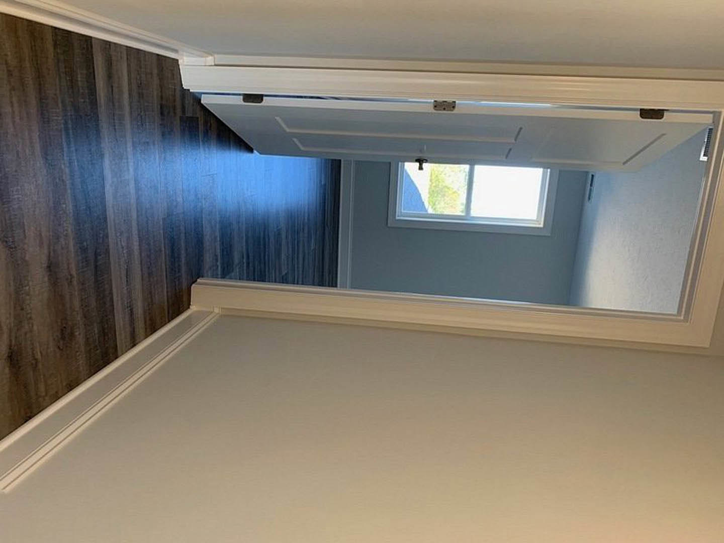 Hallway with white walls, blue ceiling, wood flooring, white door, and window with white frame and sheer curtain