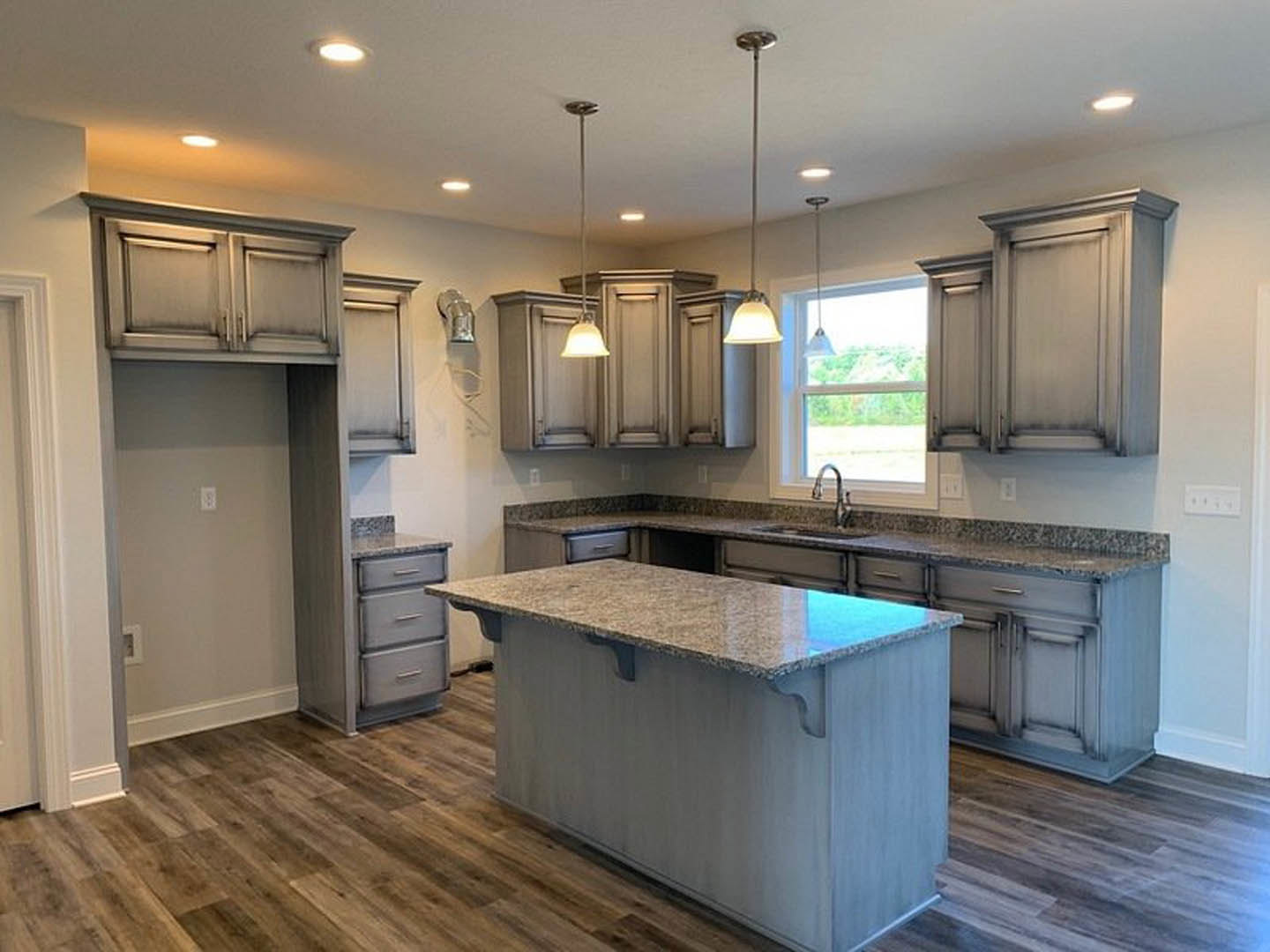 Spacious kitchen featuring a large marble-topped island, white cabinetry, stainless steel sink, hardwood flooring, and ample natural light from a window