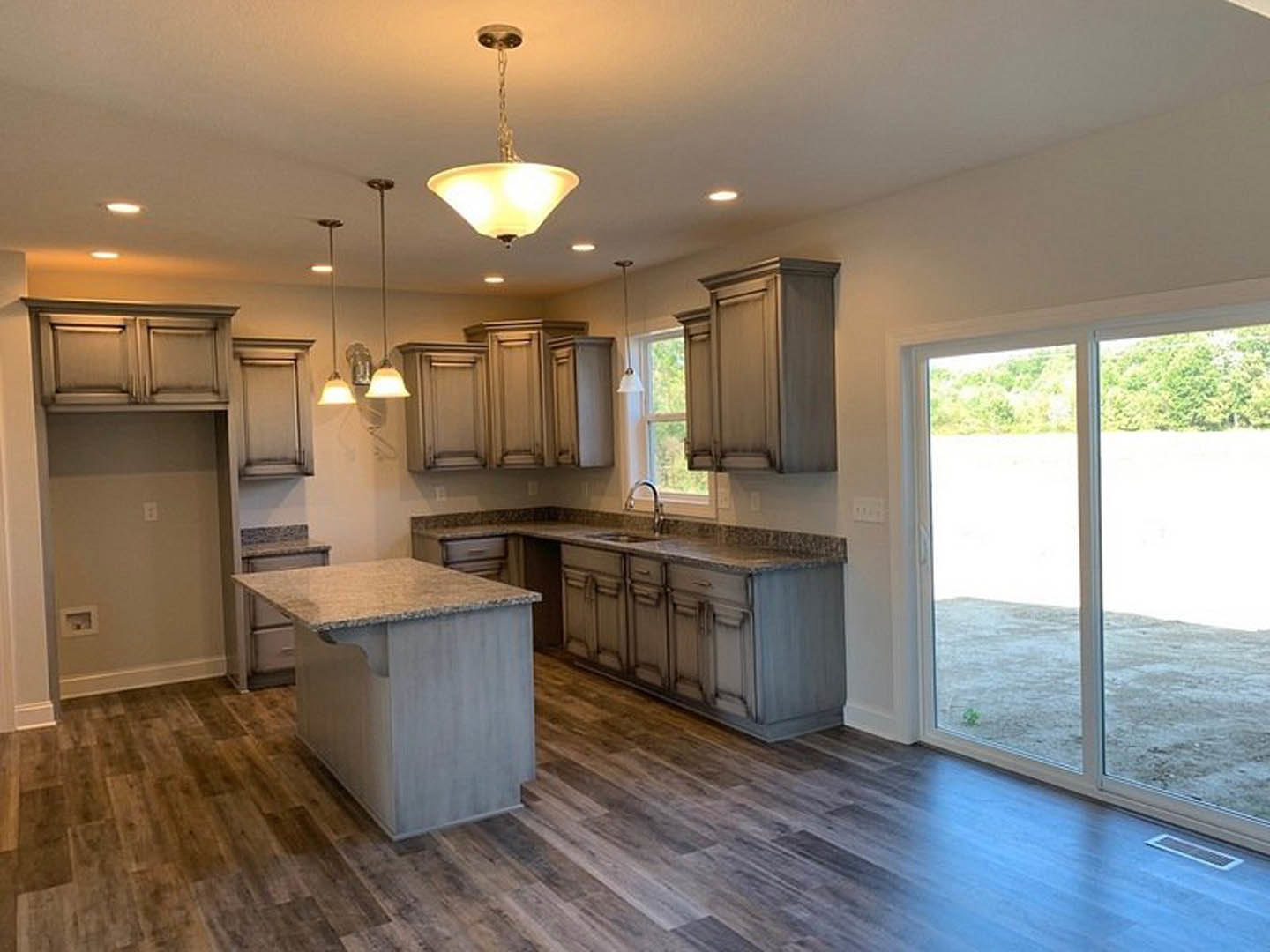 Kitchen with marble-topped island, wood flooring, white cabinetry, pendant light fixture, and sliding glass door leading outside