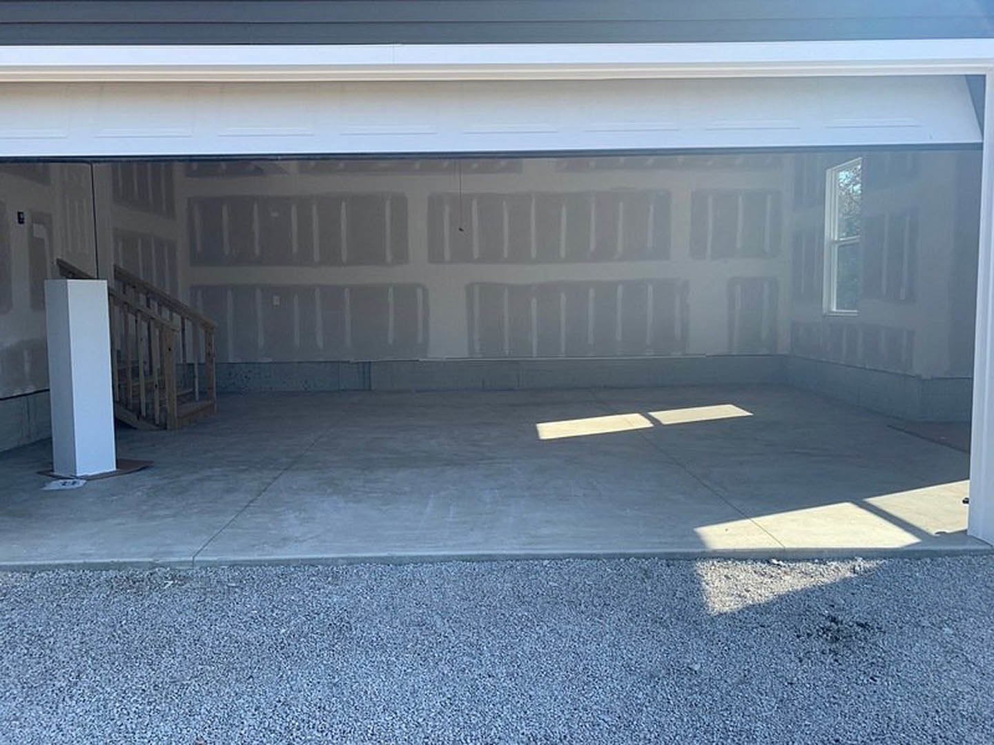 Garage interior featuring concrete flooring, white painted walls, a staircase with grey carpet, and a wooden storage box.