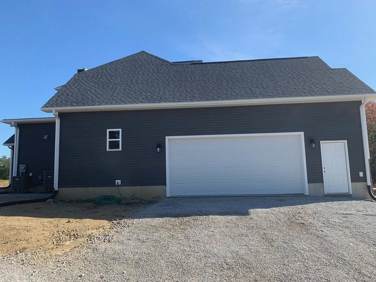 White garage door with black trim, adjacent white entry door, black siding, white-framed window, gabled roof, concrete driveway, blue sky