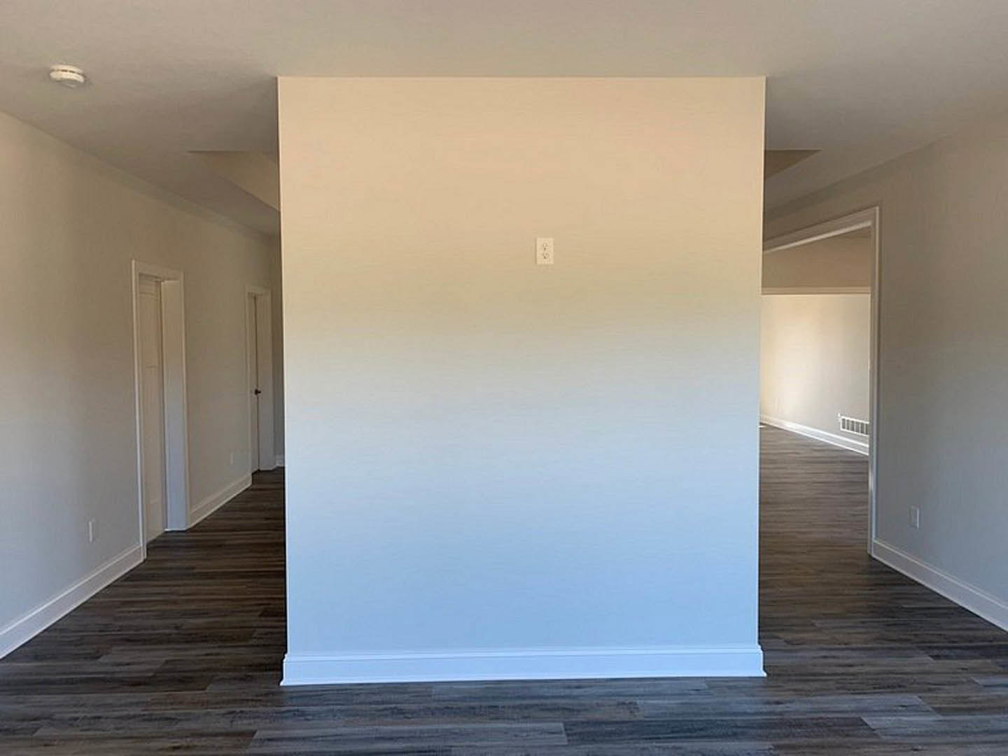 White plaster wall with light switch, wood flooring, white railing, and close-up of door with silver knob