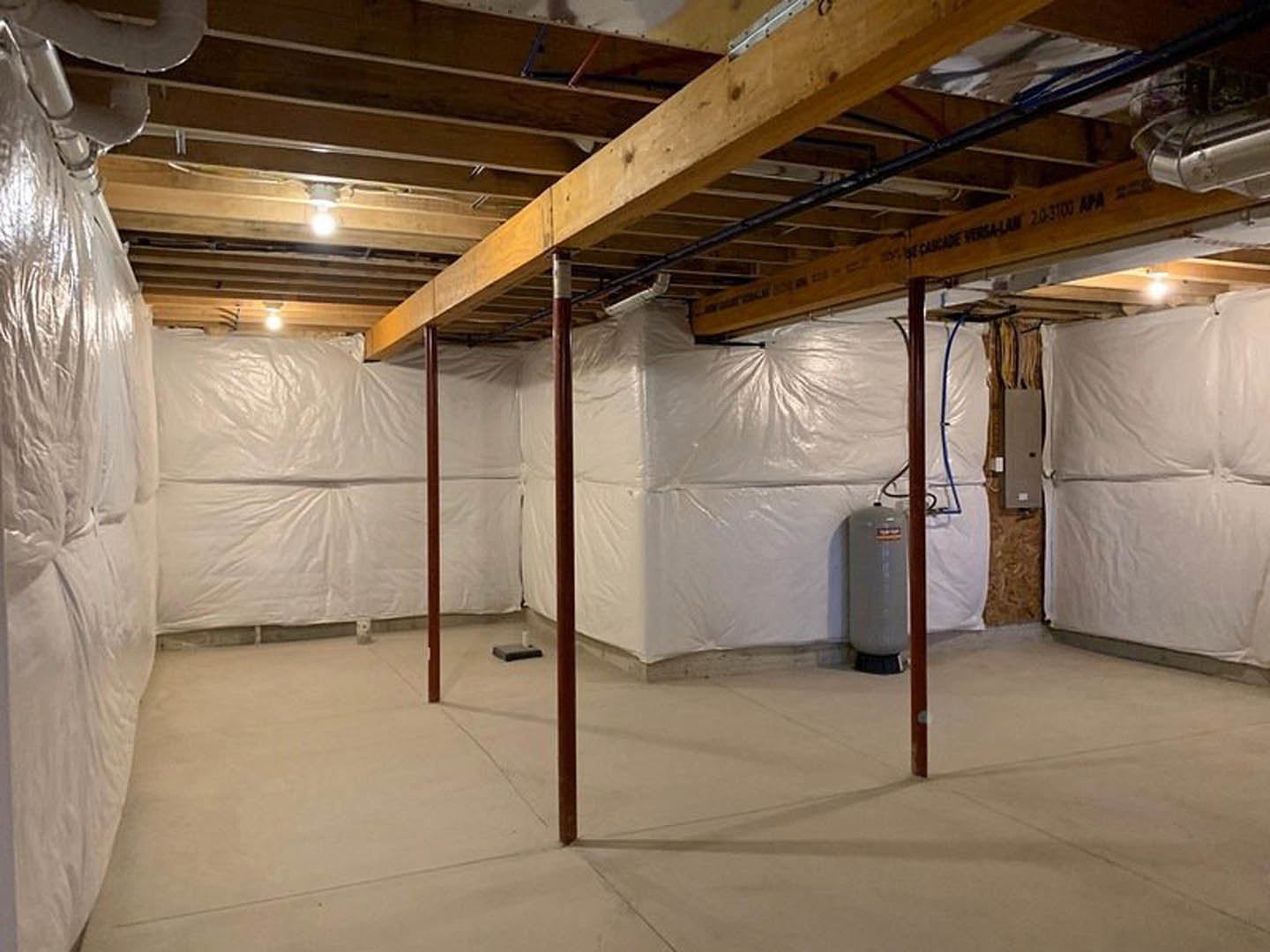 Basement with concrete floor, exposed support pole, and walls and ceiling covered in white plastic sheeting for insulation or moisture protection