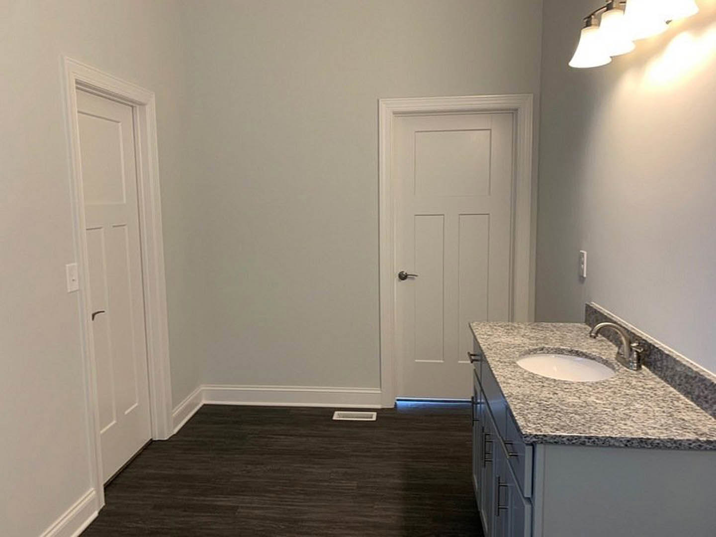 Marble countertop sink with chrome faucet, black wood floor, white baseboards, white door with silver handle, modern light fixture above