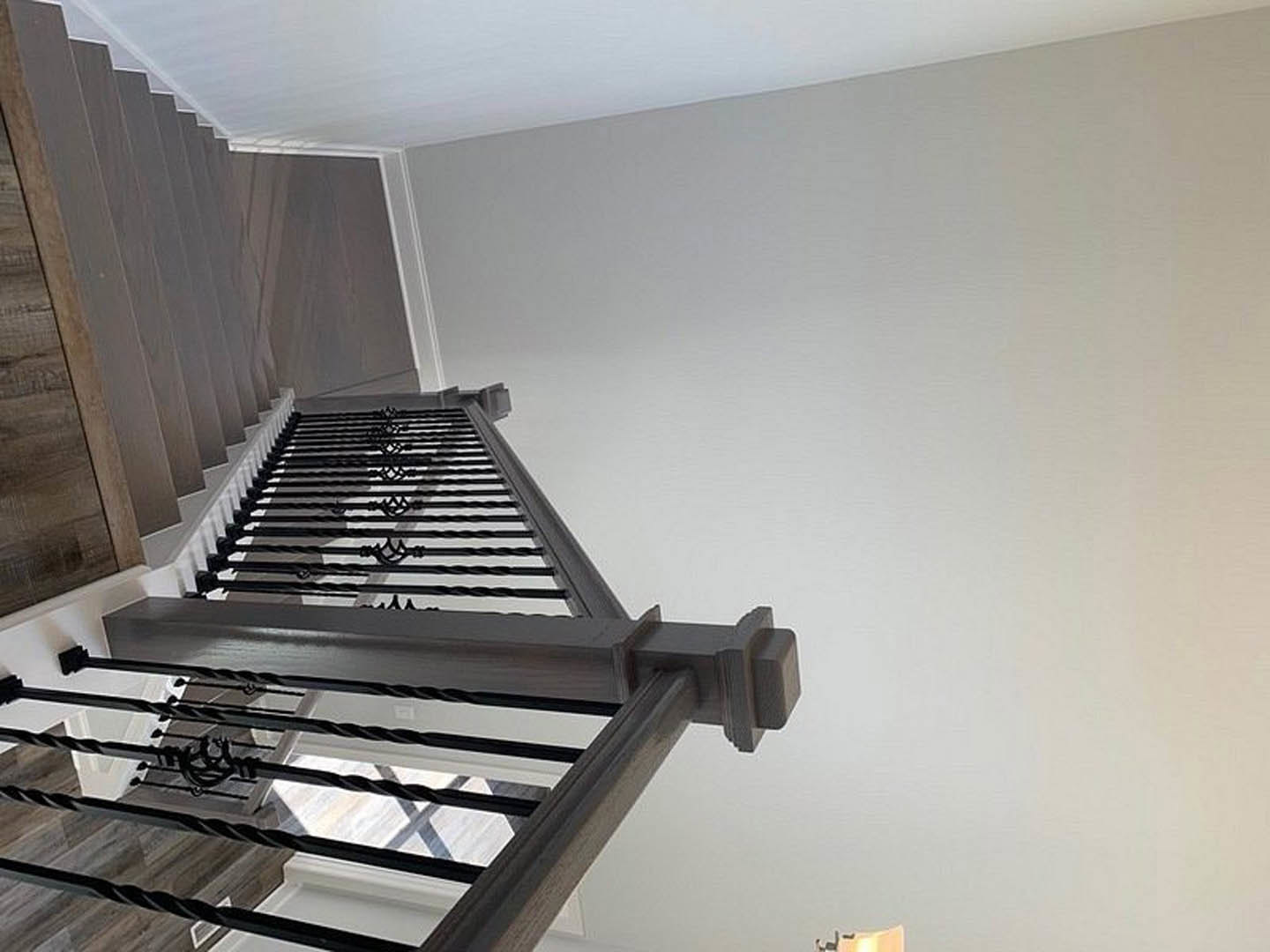 Wood staircase with black metal handrail, white plaster walls, and warm wood accent wall in modern residential interior