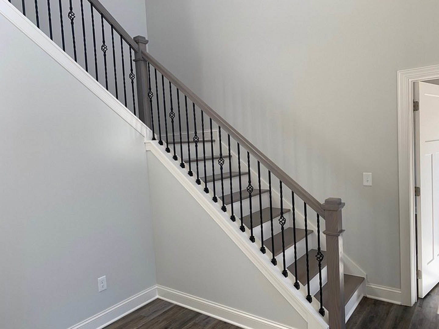 Staircase with black metal railings, white walls, white baseboards, and a white pillar