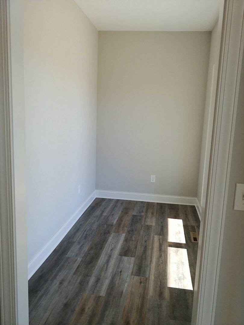 Wood flooring with natural light, white plaster walls, white door frame, and columns in a residential interior.