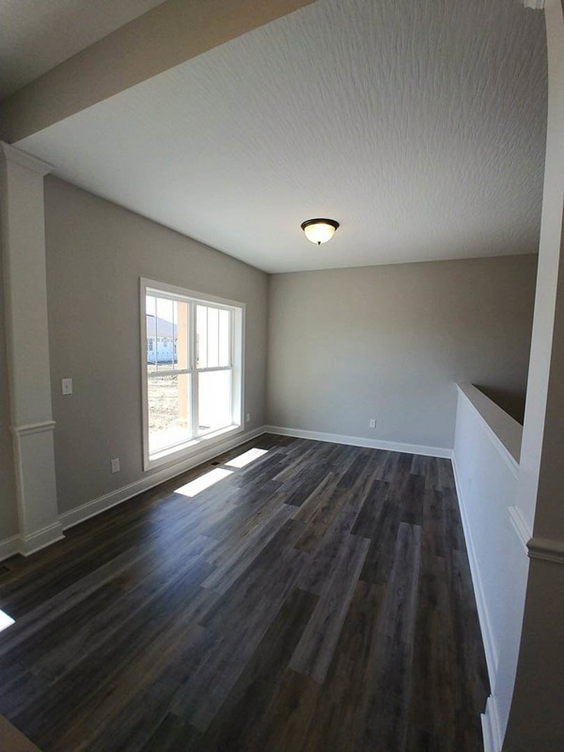 Wood flooring, white walls with black trim, large window with metal bars, ceiling-mounted light fixture