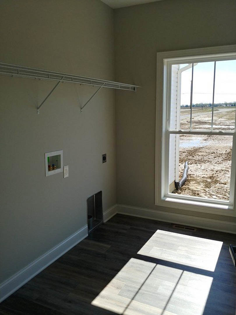 Square window with white trim overlooking a dirt field, dark wood flooring with sunlight, white tile section, and a metal trash can in a bathroom corner.