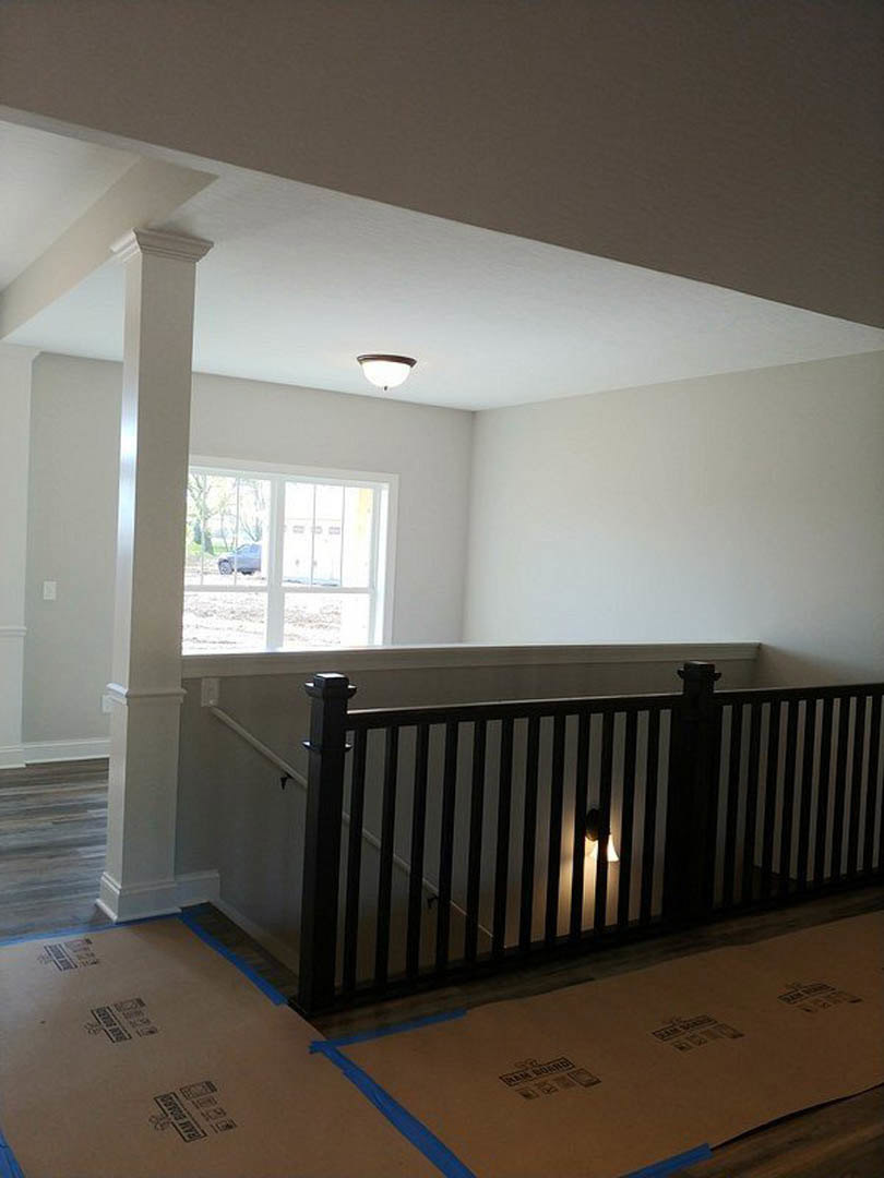 Wood staircase with white handrail and balusters, light fixture mounted on white plaster wall, open door leading to adjacent room, cardboard box with blue tape resting on hardwood
