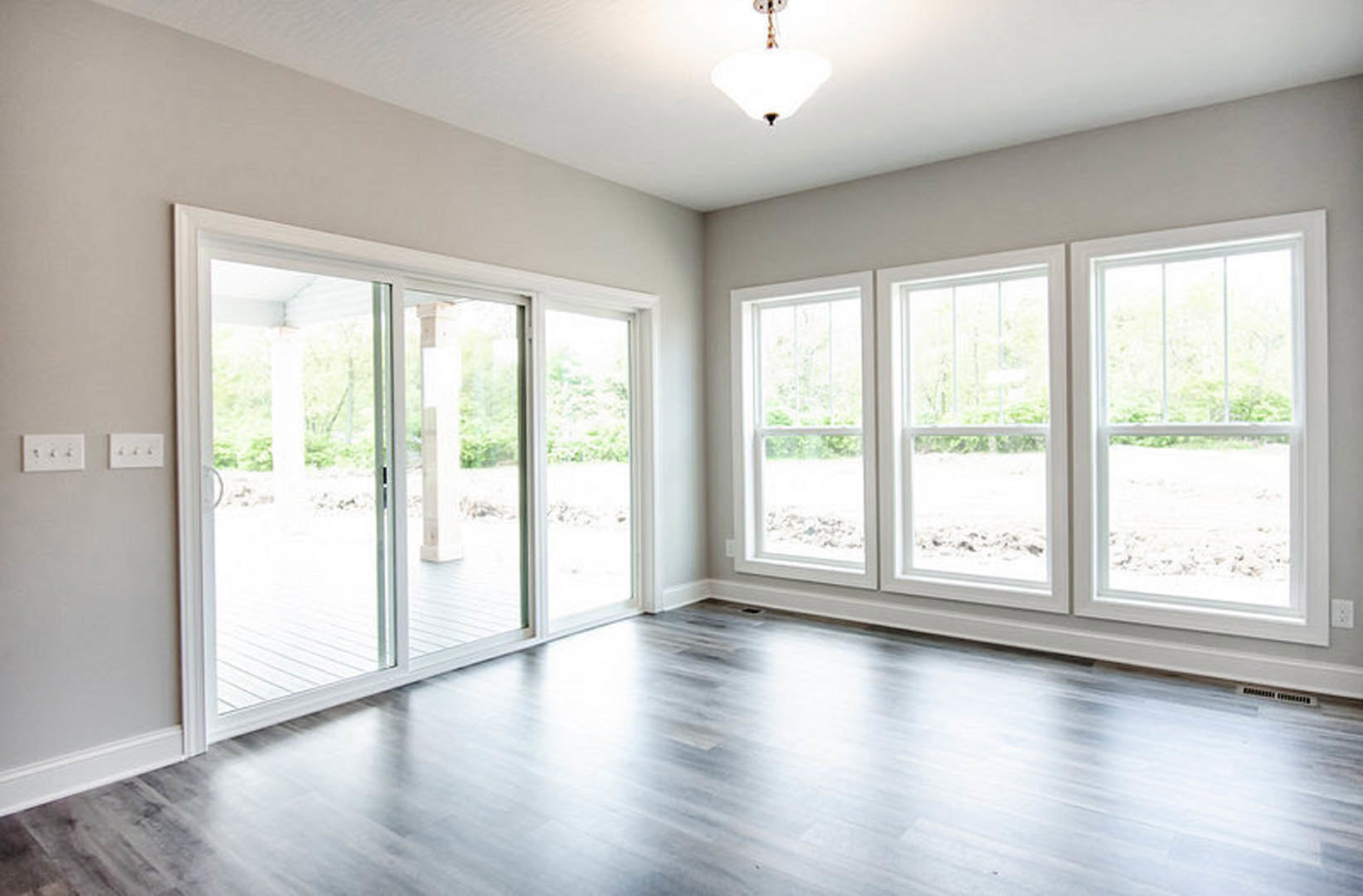 Wood flooring and white walls in a bright room featuring a sliding glass door, row of windows, and modern light fixture above a white surface with multiple knobs