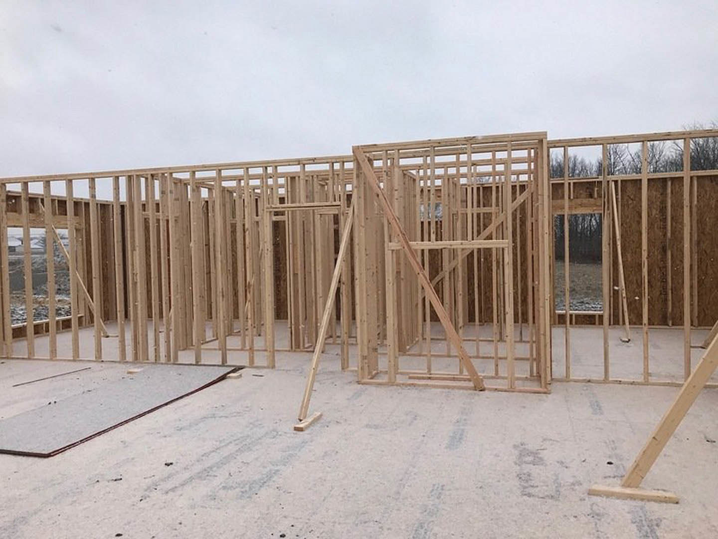 Wood-framed house under construction with exposed beams, concrete floor, and blue sky in background