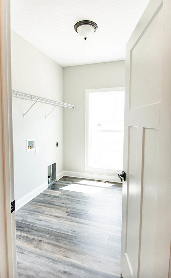 Wood plank flooring, white paneled door with glass window, white walls, ceiling light fixture