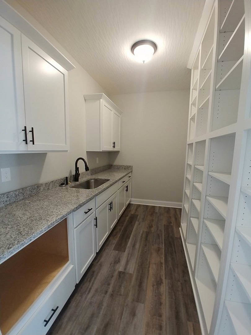 White kitchen cabinets with marble countertops, stainless steel sink and faucet, black metal bar handle, tile backsplash, ceiling light fixture, and open shelving.