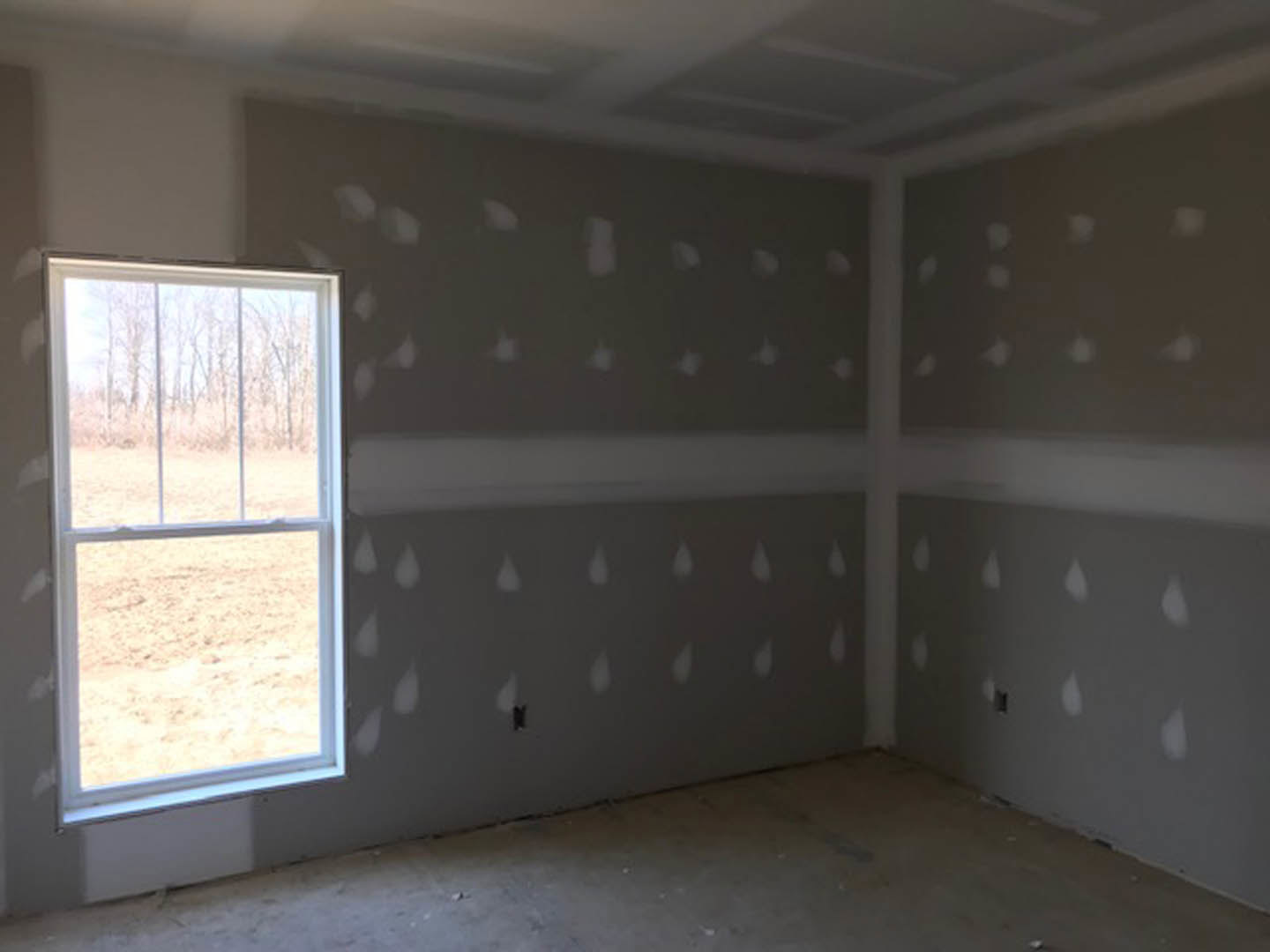 White-painted walls, large window overlooking green trees, grey flooring, minimal furnishings