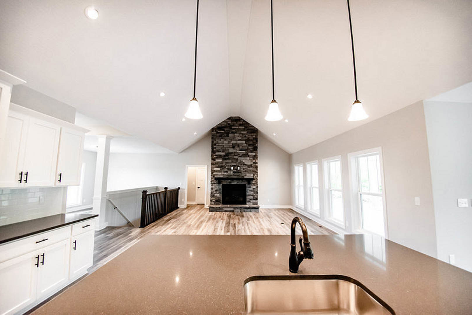 Open kitchen with white cabinetry, stone countertops, stainless steel appliances, and a built-in fireplace along one wall