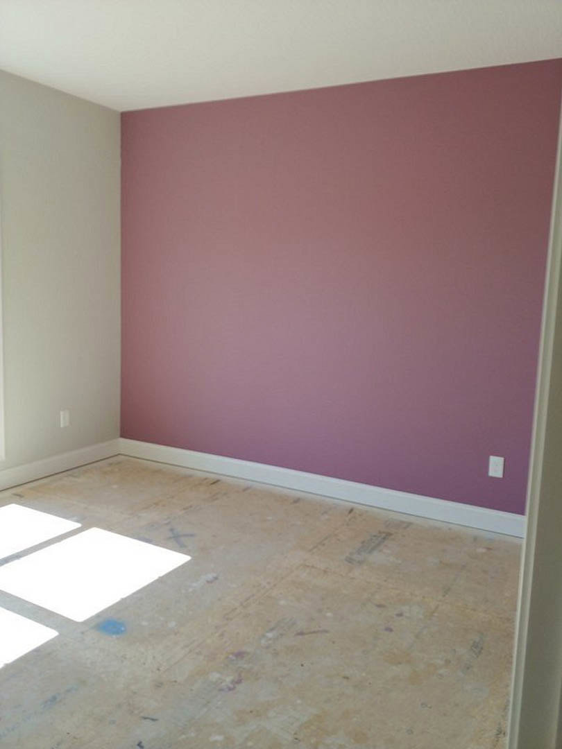Room with purple accent wall, white surrounding walls, light-colored flooring, and a blue paint stain near the baseboard