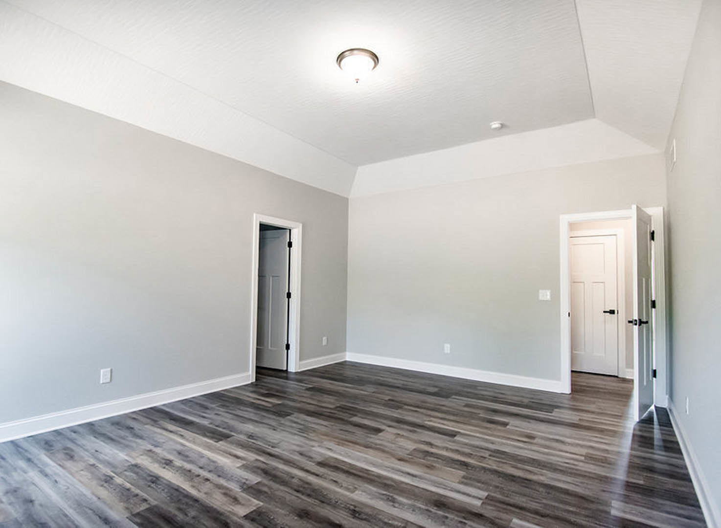 Wood flooring in a room with white plaster walls, white door featuring a black handle and overhead light fixture