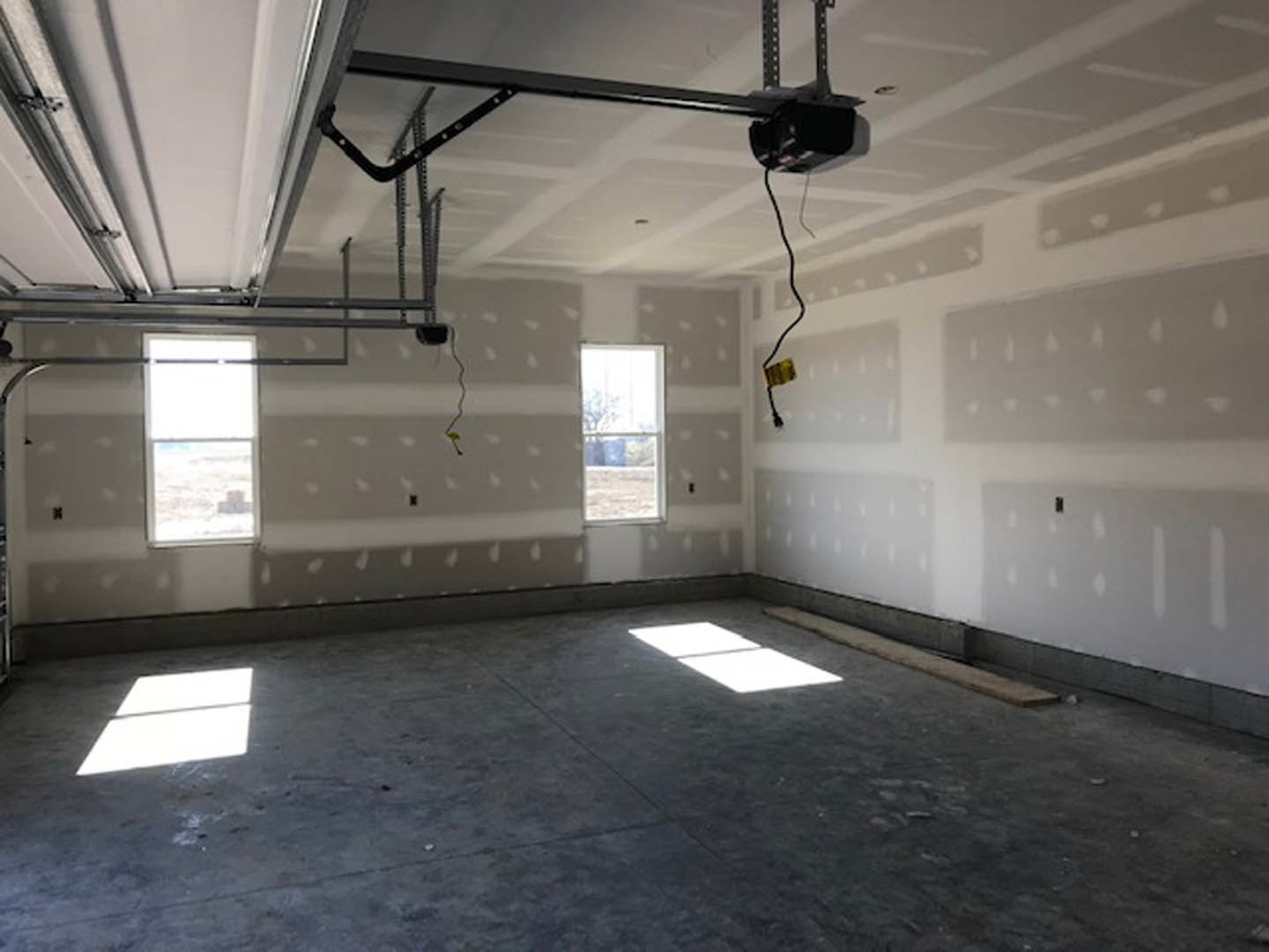 Spacious garage with plaster walls, white-framed window, ceiling fixture, and concrete floor illuminated by daylight.