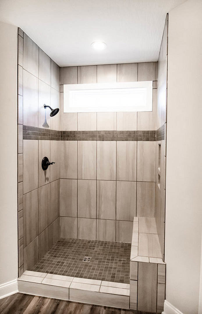 Walk-in shower with chrome shower head, white subway tile walls, glass enclosure, and light gray tile flooring