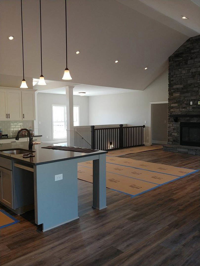 Open kitchen with granite countertops, stainless steel sink, white cabinetry, built-in fireplace, black metal railing with integrated lighting, rectangular black-framed appliance