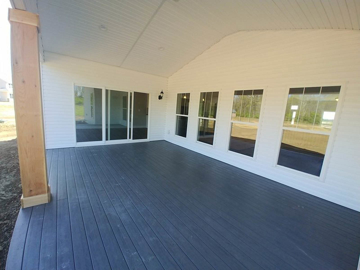 White exterior home with numerous large windows, black deck, glass doors with white frames, wooden post, and illuminated interior visible through windows.