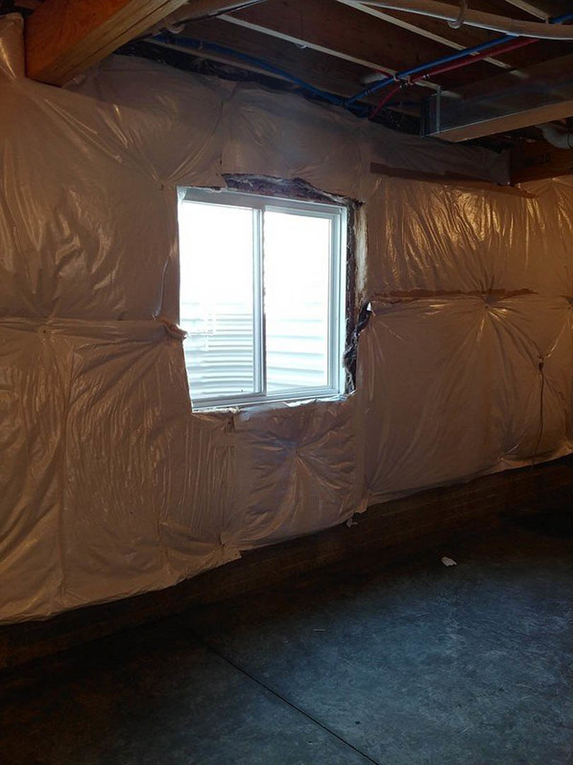 White-framed window in unfinished room, concrete floor partially covered with white plastic sheet, exposed ceiling with blue pipes, person standing near window