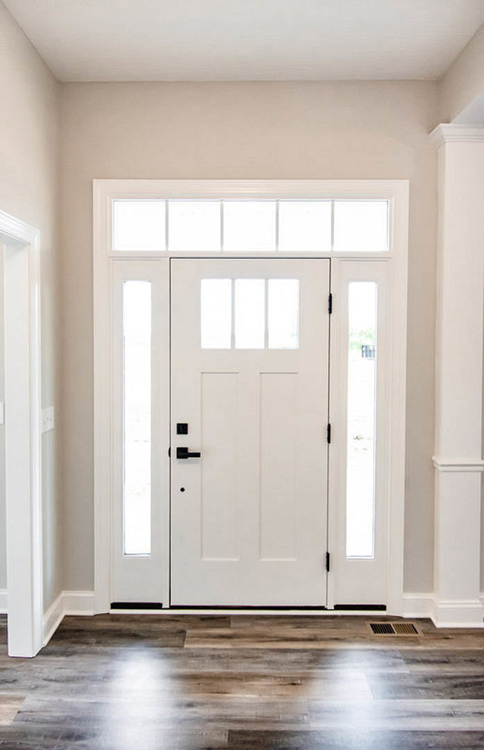 White door with glass panes and black handle, wood floor reflecting light, white wall with black trim