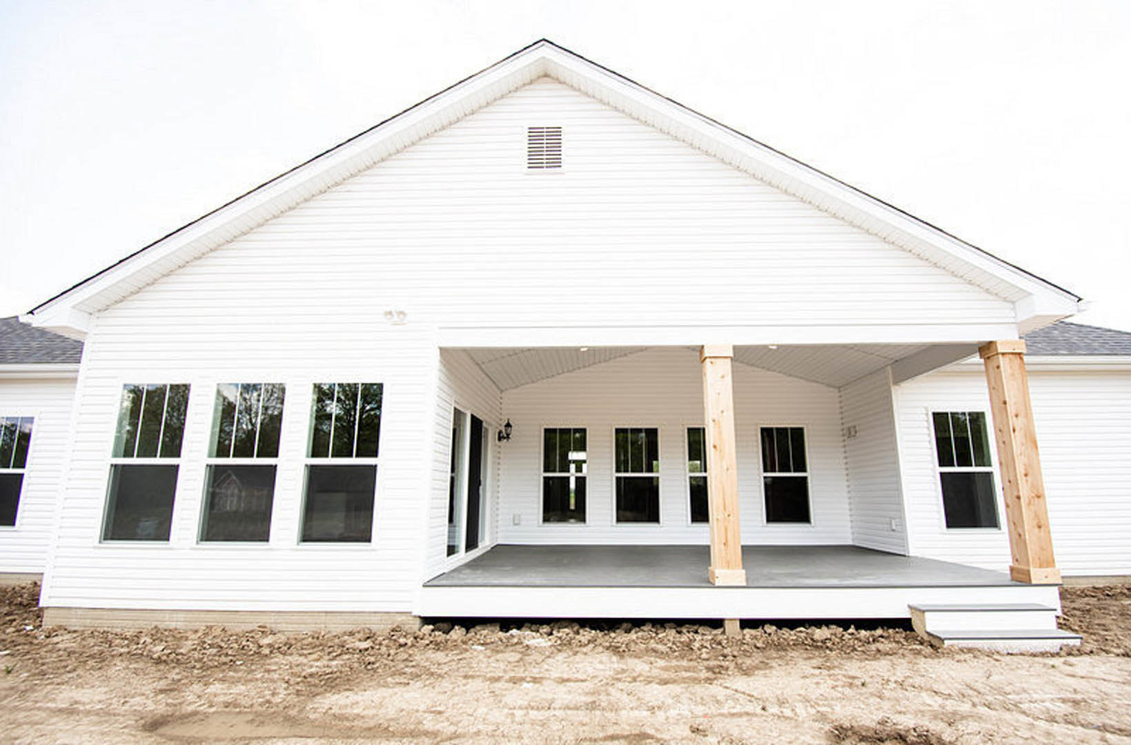 White siding house with covered porch, wooden posts on concrete, large windows, and stone landscaping under blue sky