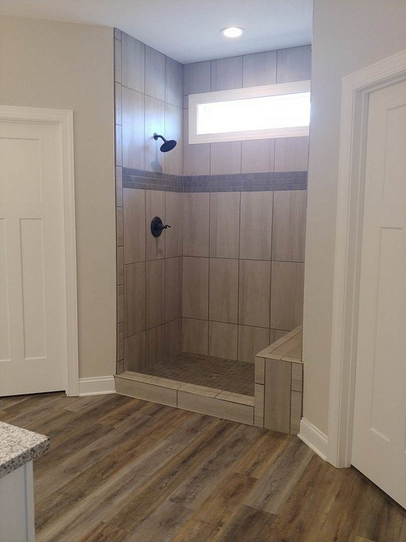 Glass shower enclosure with chrome hardware, white tile walls, wood plank flooring, white door, and quartz bathroom countertop