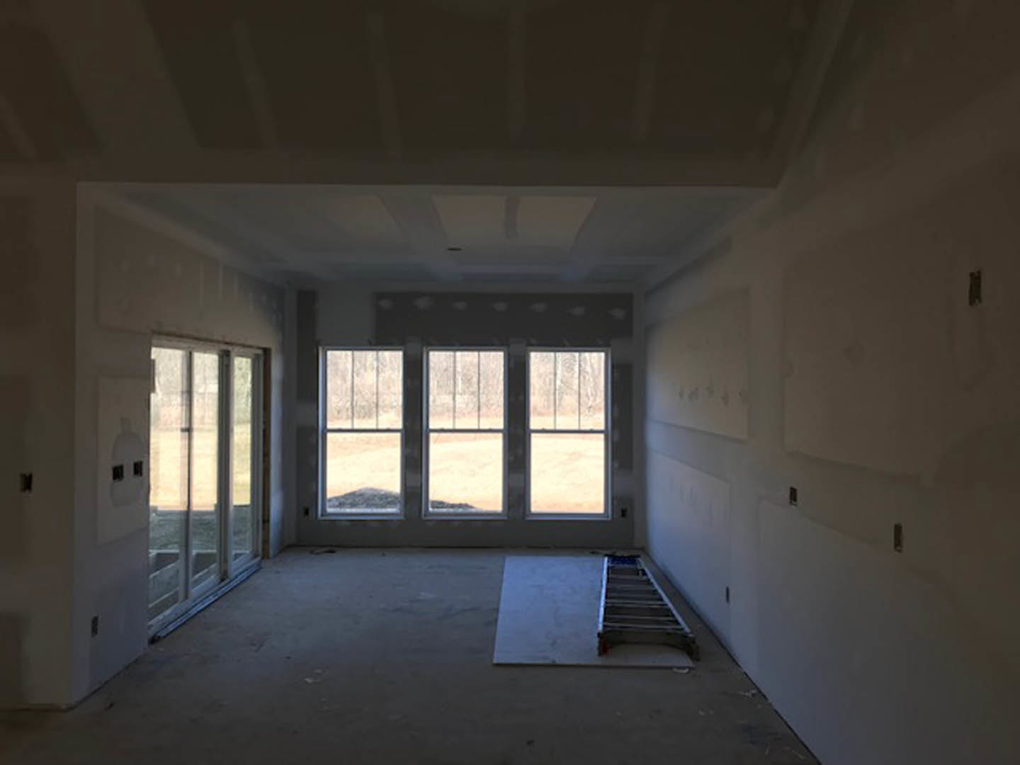 Bright room with multiple tall windows, white plaster walls, wood floor, metal ladder leaning against the wall, and simple ceiling detailing