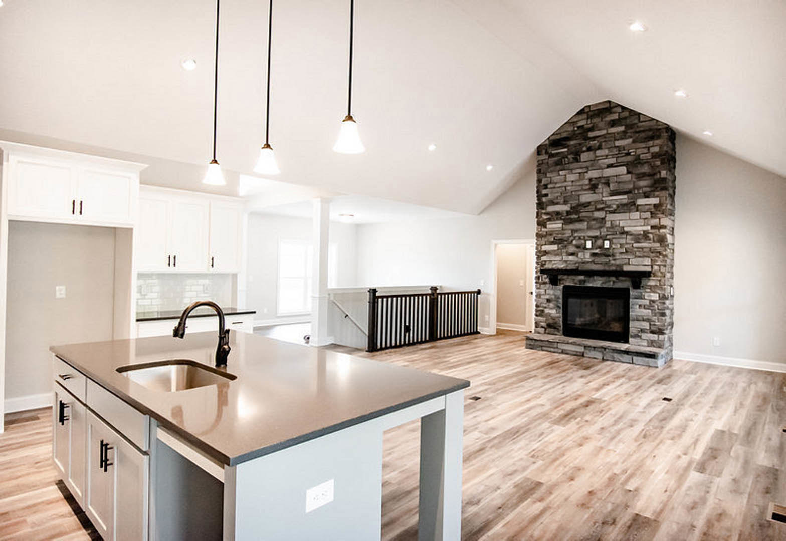 Open kitchen with light cabinetry, stone fireplace featuring a black mantel, stainless steel microwave, undermount sink set in a stone countertop, hardwood flooring