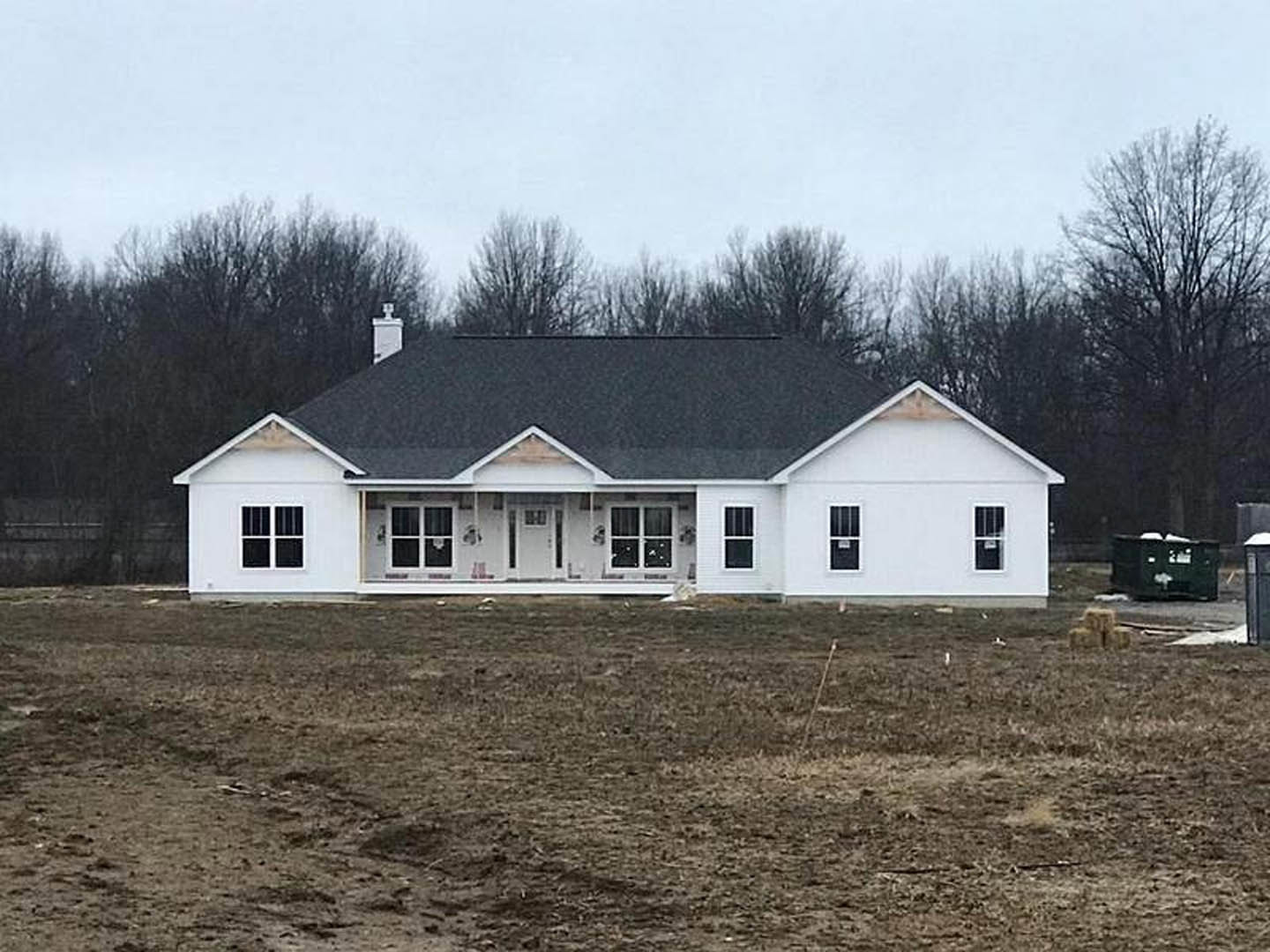 Partially built house with black roof, white framed windows, and brown dirt lot, surrounded by trees under a clear sky