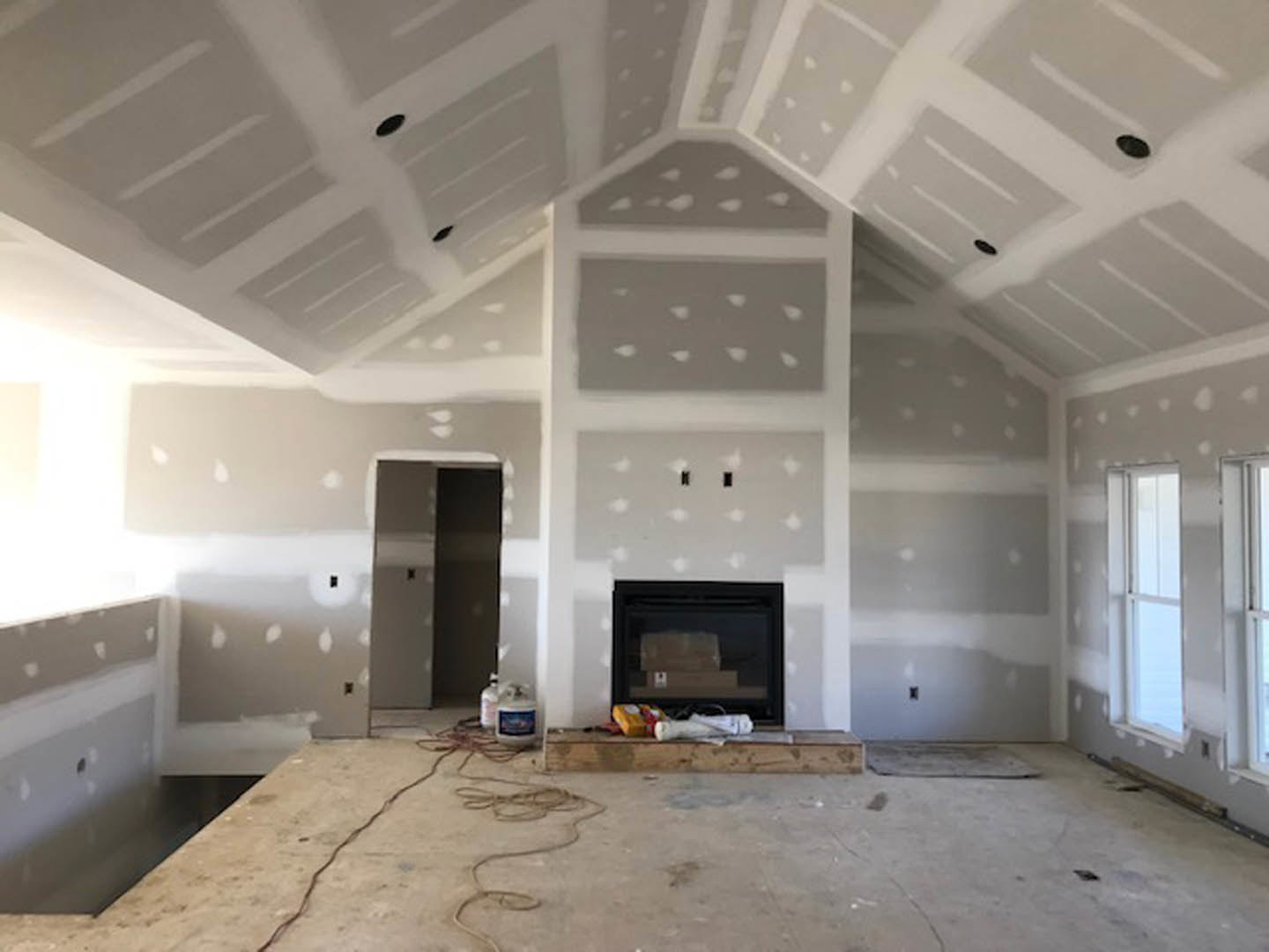 Living room with plaster ceiling, exposed wood beams, black fireplace, light wood flooring, and large windows