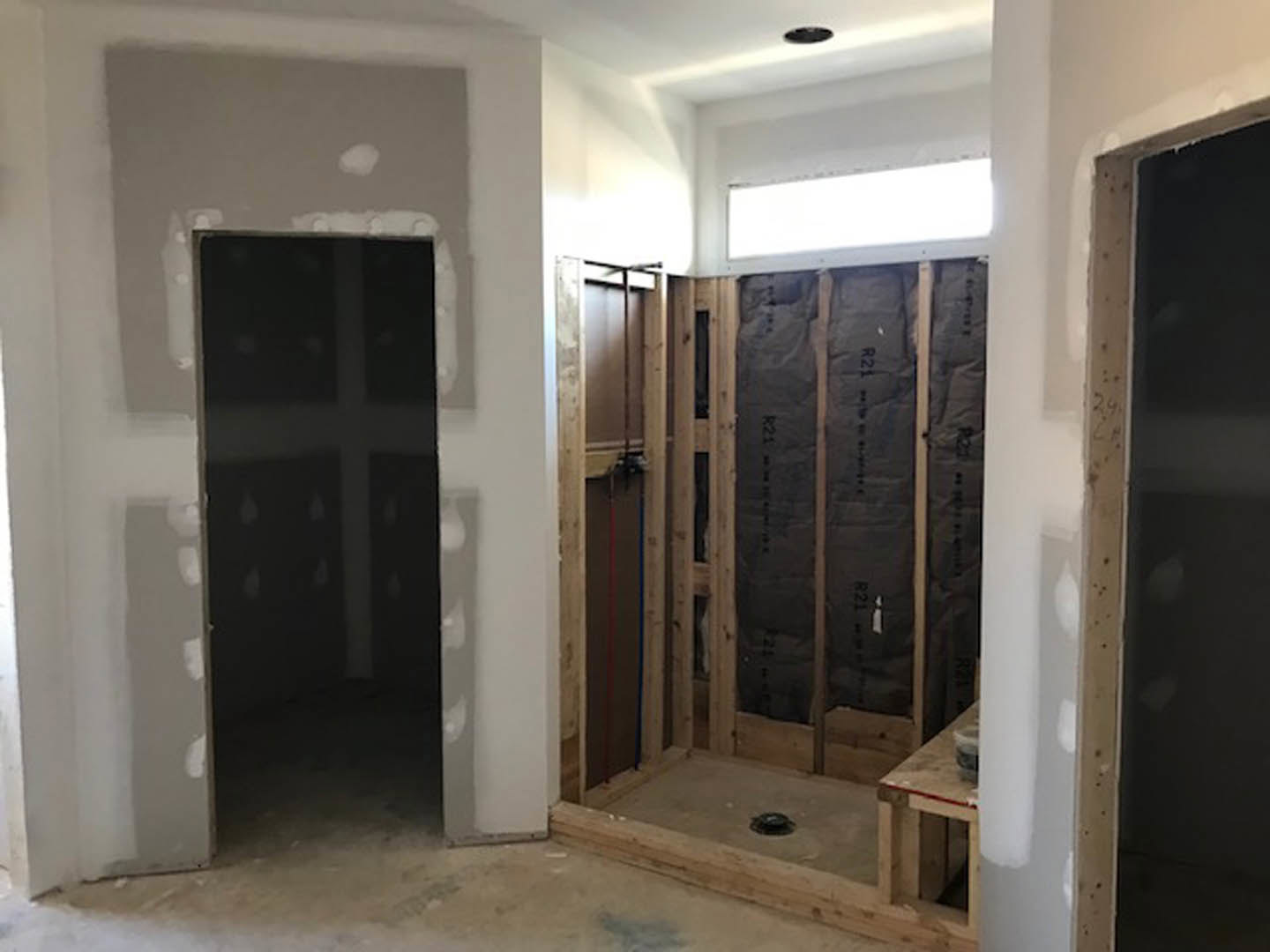Modern bathroom featuring a glass shower enclosure, wooden door, light plaster walls, wood flooring, and recessed ceiling lighting.