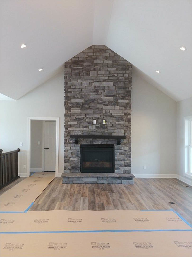 Modern black wood-burning stove with glass window and black shelf, white door with black handle, black radiator, light wood flooring, cardboard box with blue tape, white walls and
