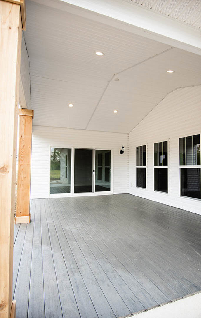 White siding house with large windows, wooden deck, white-framed door, and tree shading the porch