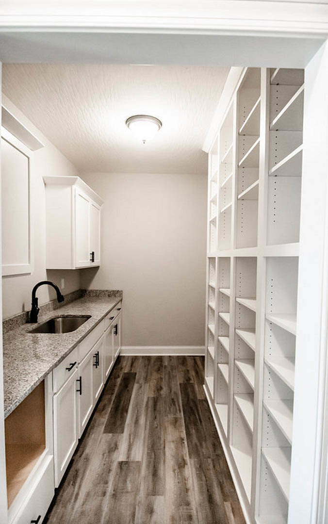 White kitchen cabinets and open shelves, light countertops, stainless sink, wood flooring, and neutral wall paint.