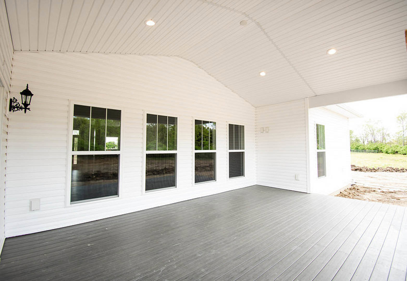 White exterior home with multiple large windows, wooden flooring visible through open doorway, white walls and ceiling, glass window panes, porch area at entrance.