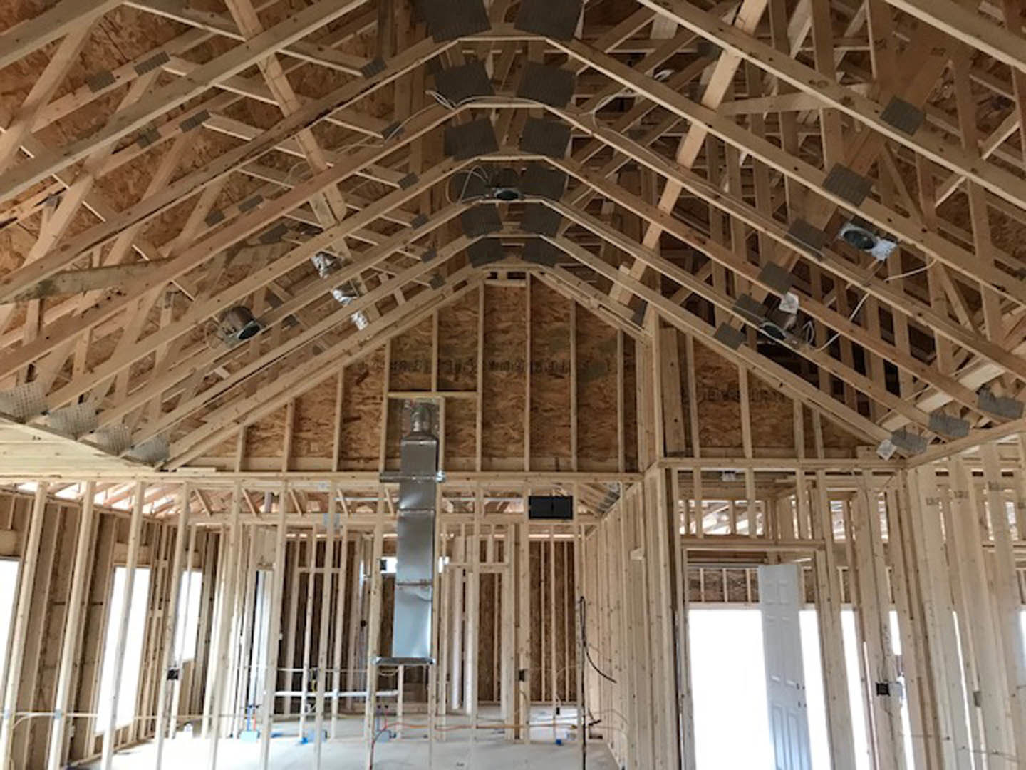 Exposed wood framing and ceiling beams in a partially constructed home interior, with black wall panels featuring white borders and a white door illuminated by natural light