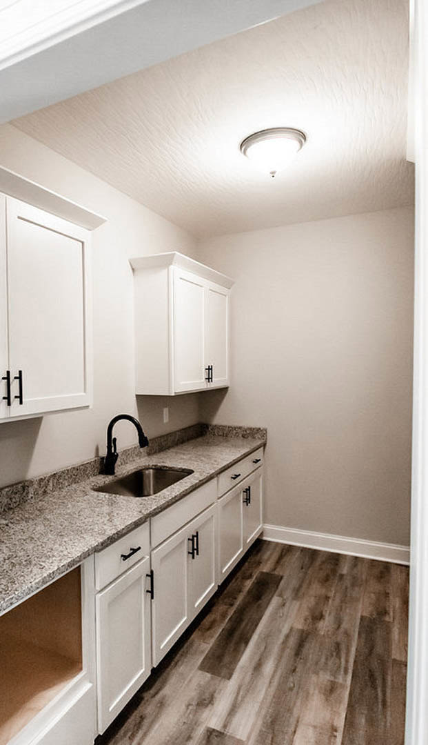 White kitchen cabinets, stainless steel sink, light tile backsplash, stone countertop, wood flooring, built-in appliances