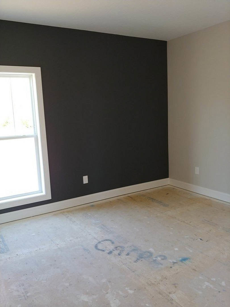 Concrete floor with handwritten markings, black accent wall, large window framed in black, white wall with black trim, architectural blueprint visible on floor.